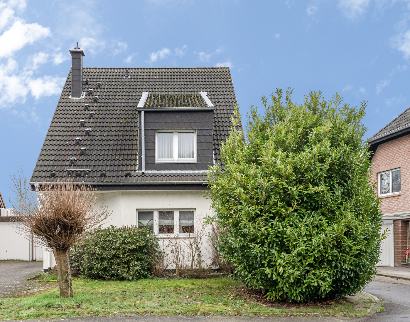 Vorderansicht eines Einfamilienhauses mit großem Busch und kurzem Baum im Vorgarten.