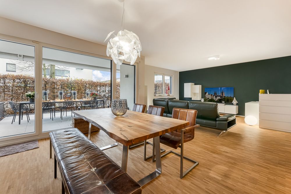 Modernes Wohnzimmer mit Essbereich, Holztisch, Ledermöbeln und Zugang zur Terrasse mit Gartentisch.