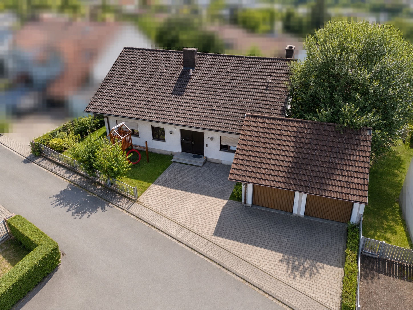 Luftbild eines Einfamilienhauses mit Garten und Doppelgarage an einer Straße.