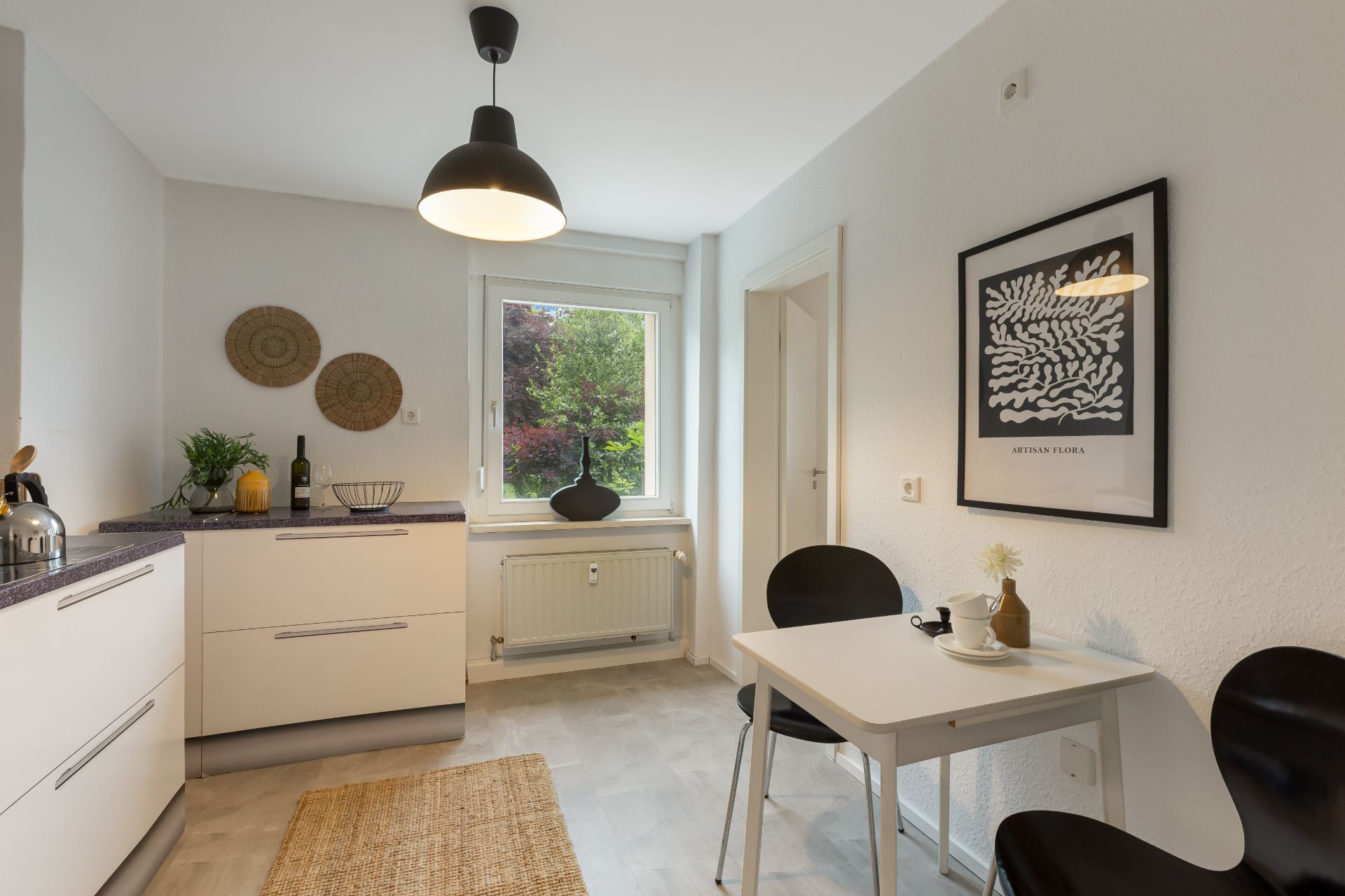 Moderne helle Küche mit Esstisch, zwei Stühlen, Fenster und Wanddekoration.