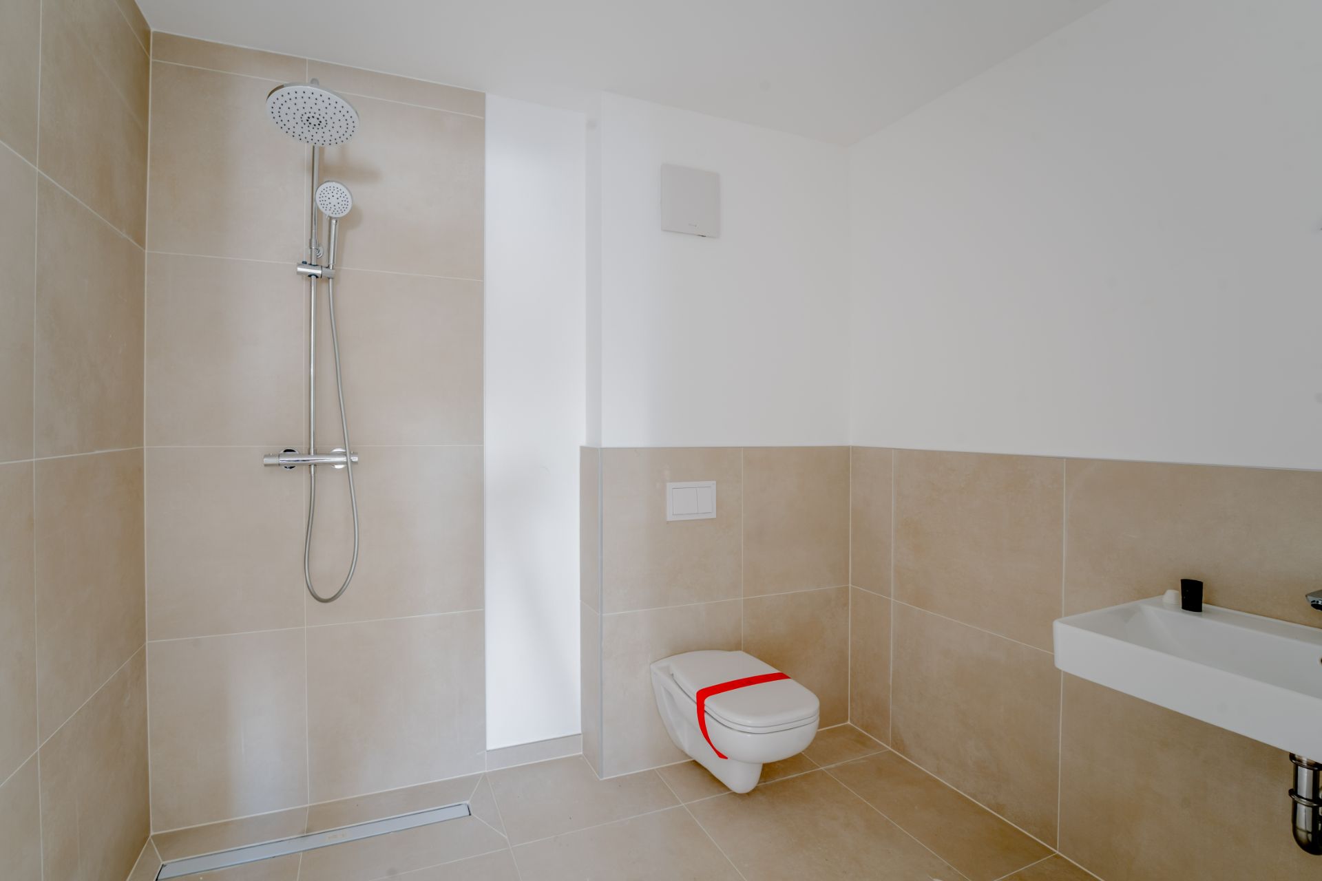 Modernes Badezimmer mit bodengleicher Dusche, Wand-WC mit rotem Band und Waschbecken.