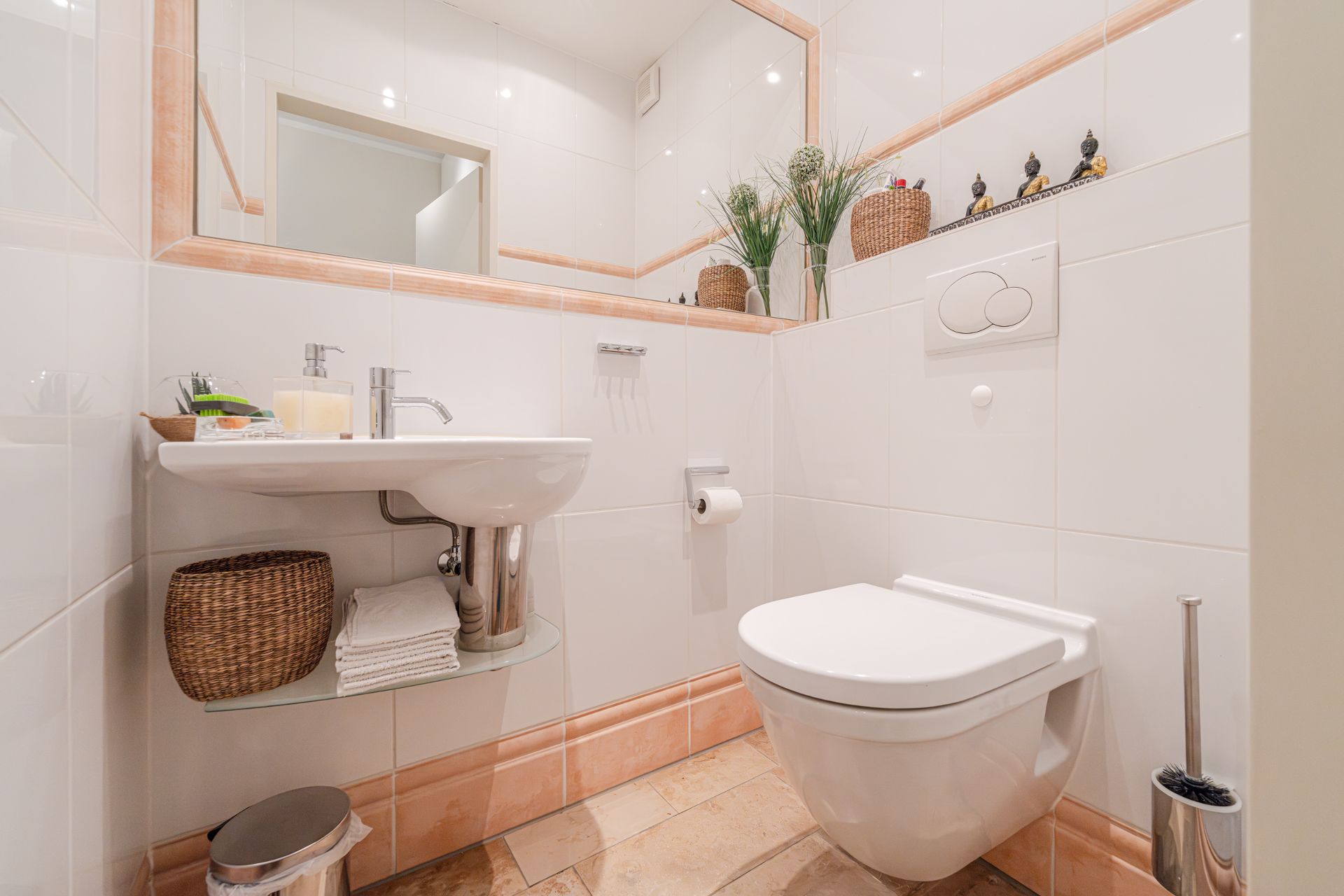 Modernes Badezimmer mit Wandtoilette, Waschbecken, Spiegel und Dekoration auf weiß gefliesten Wänden.