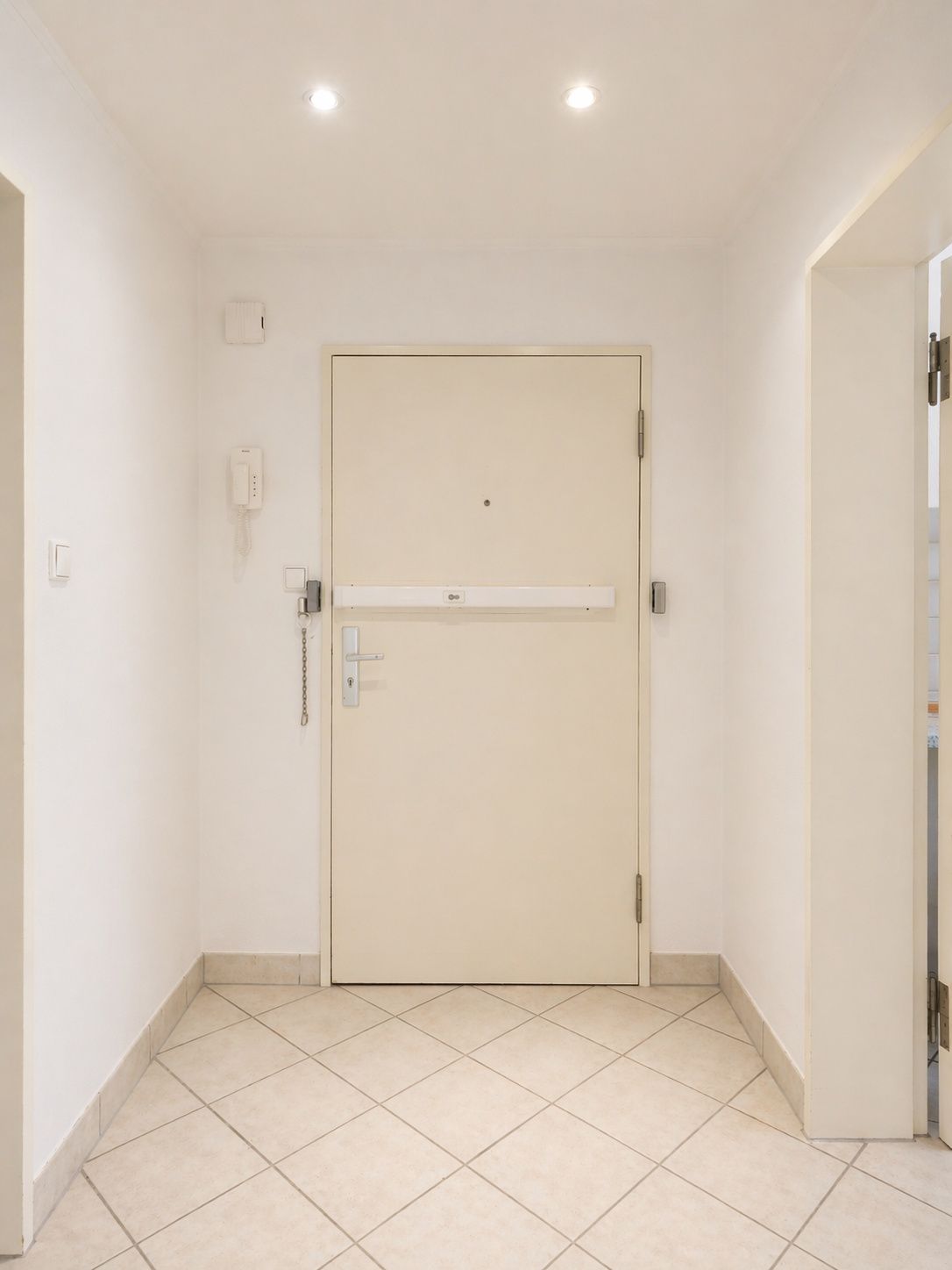 Flur mit heller Haustür, Fliesenboden und Gegensprechanlage an der Wand.