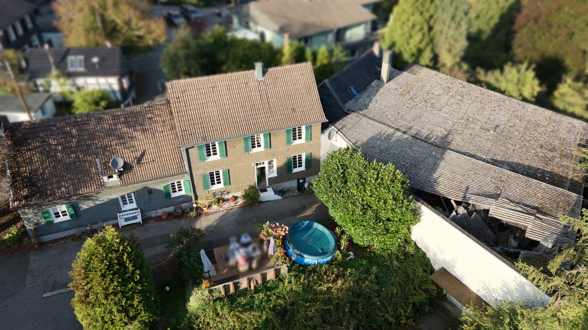 Luftaufnahme eines Wohnhauses mit grünem Garten und kleinem runden Pool im Hof.