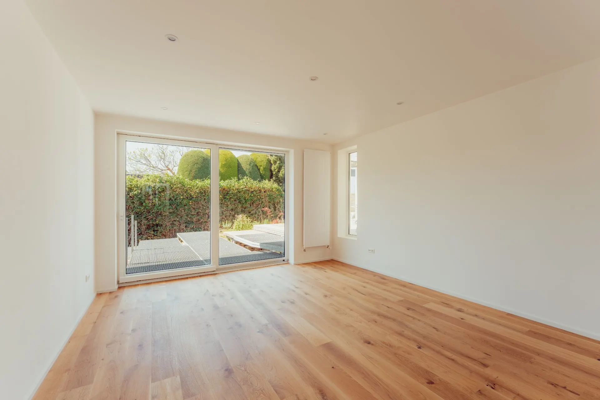 Leeres Zimmer mit Holzfußboden und großer Glasschiebetür zum Garten.