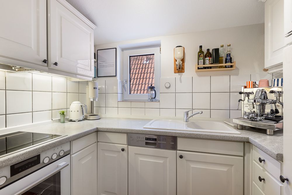 Moderne, helle Einbauküche mit weißen Schränken, Herd, Spüle und Kaffeemaschine.