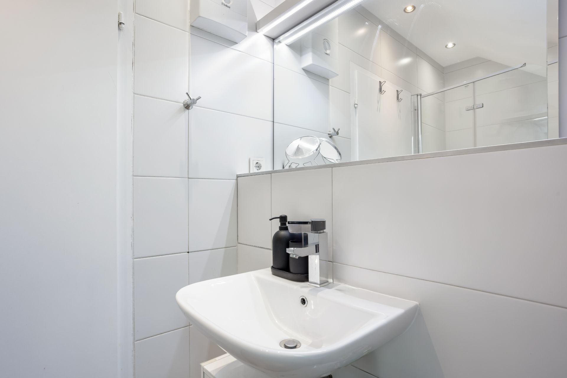 Modernes Badezimmer mit weißem Waschbecken, großem Spiegel und Seifenspendern.