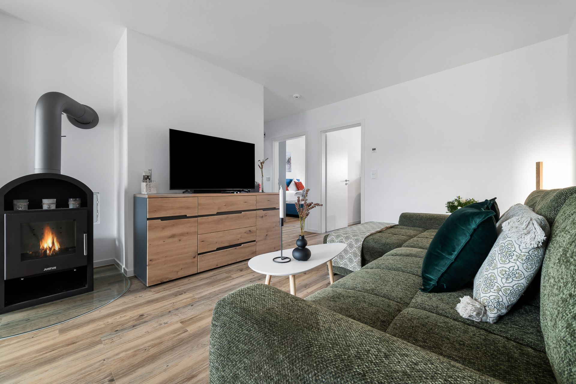 Modernes Wohnzimmer mit grünem Sofa, Kamin, Fernseher auf Holzkommode und kleinem weißen Tisch.