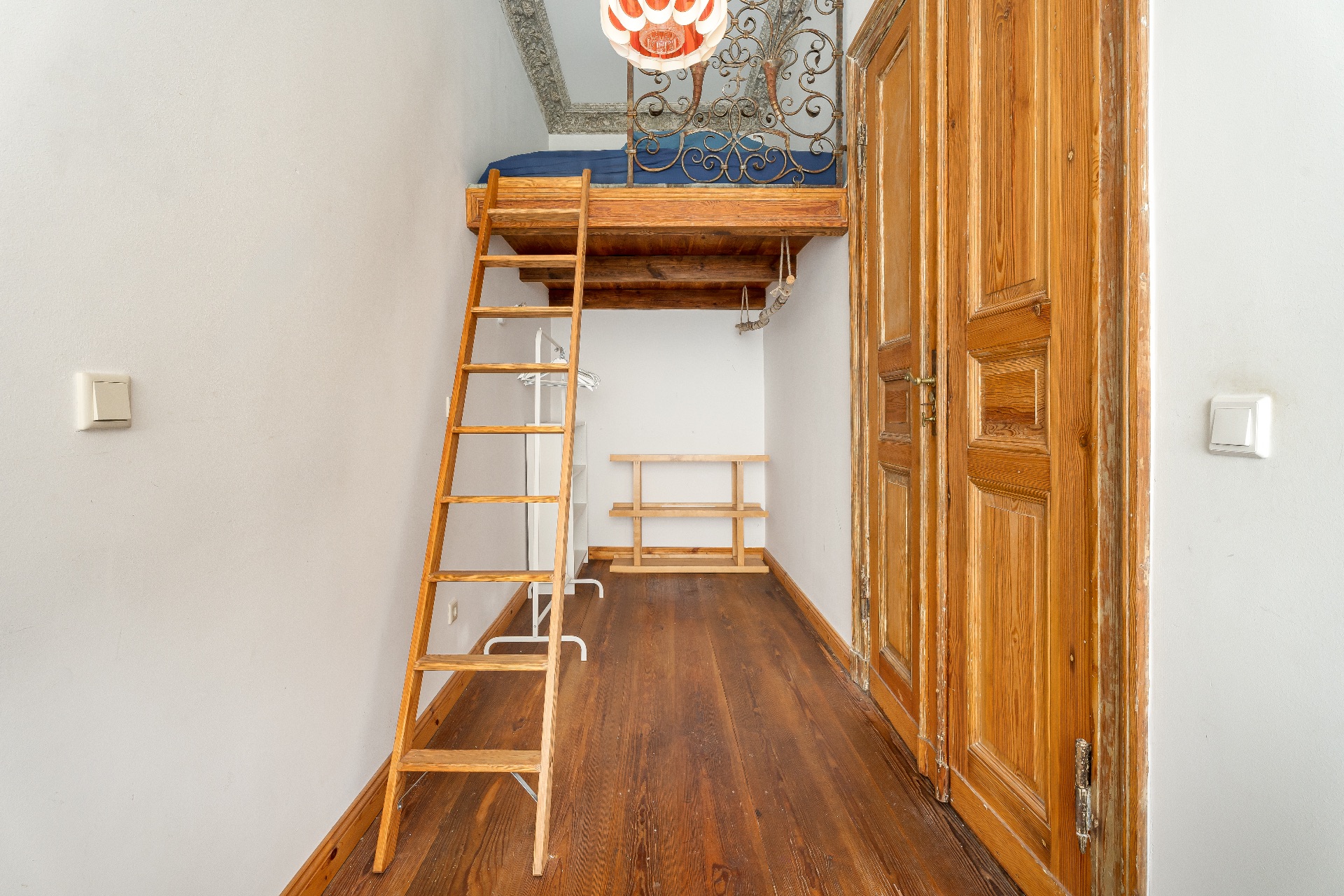 Schmales Zimmer mit Holzleiter zu einer Schlafempore und Holzboden.
