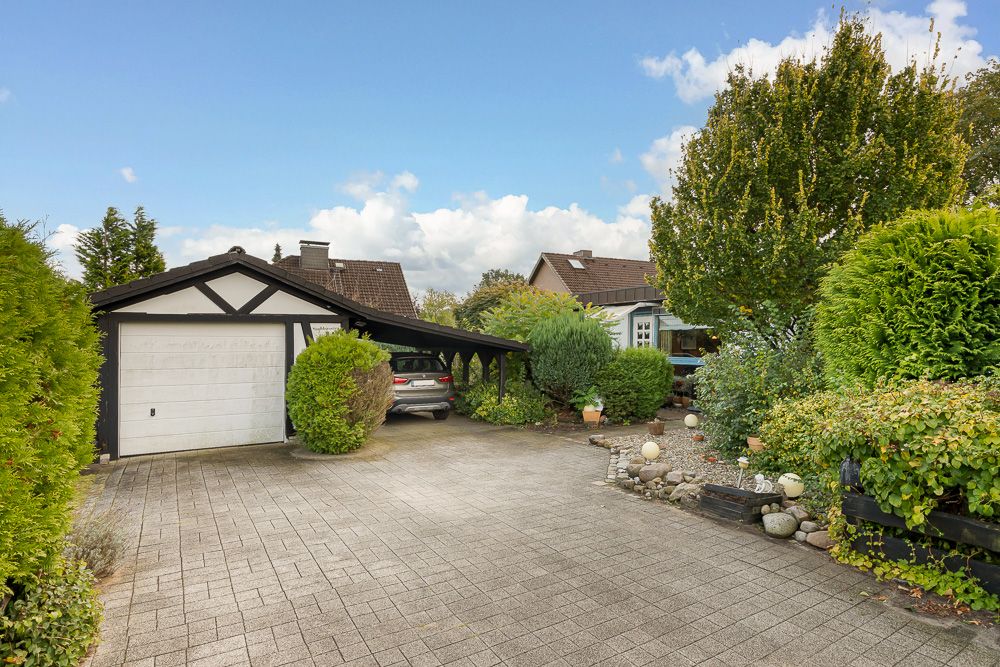 Einfamilienhaus mit Garage, Carport und bepflanztem Vorgarten bei Tageslicht.