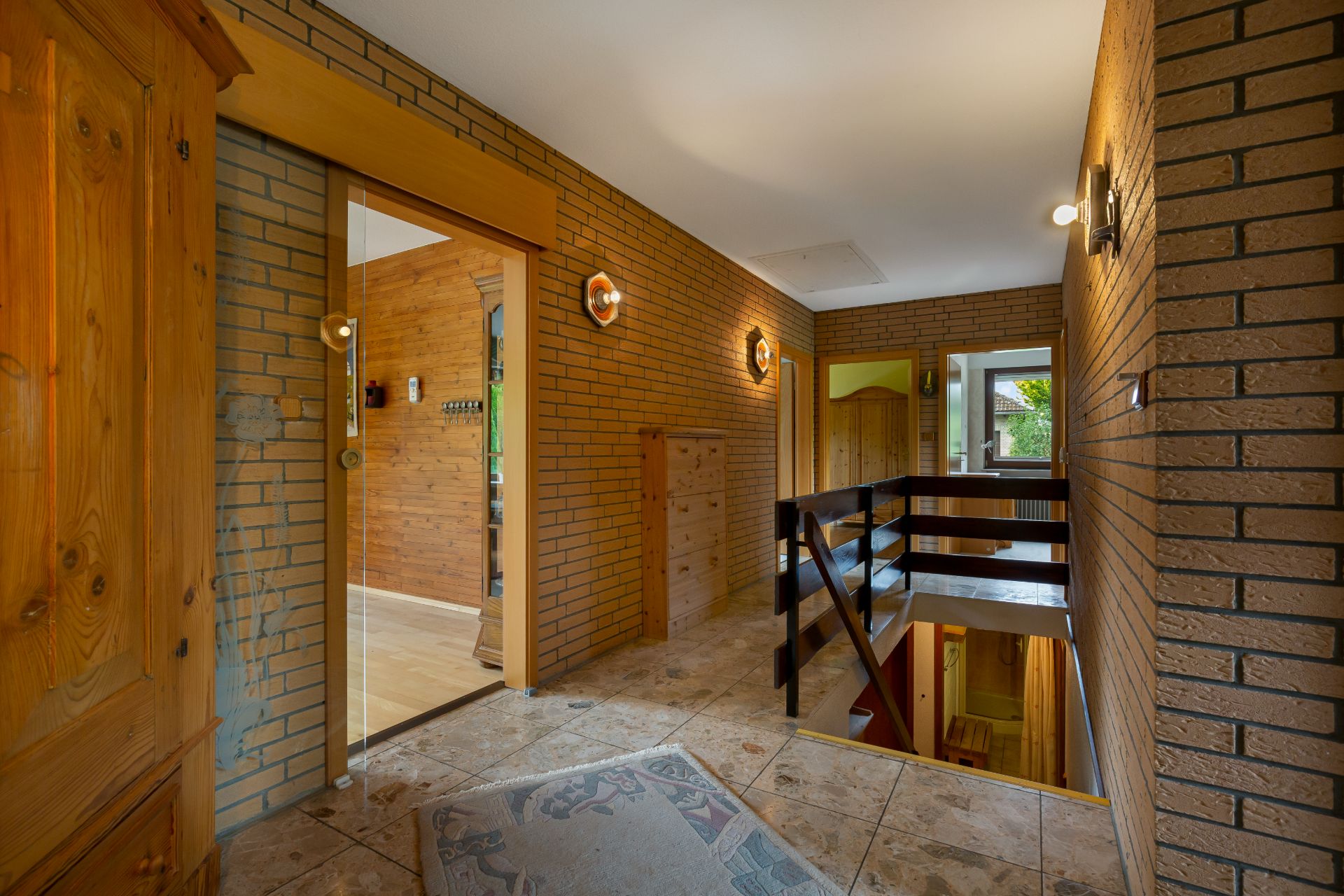 Flur mit Fliesenboden, Holzkommode, Treppe und sichtbaren Ziegelwänden in einem Wohnhaus.