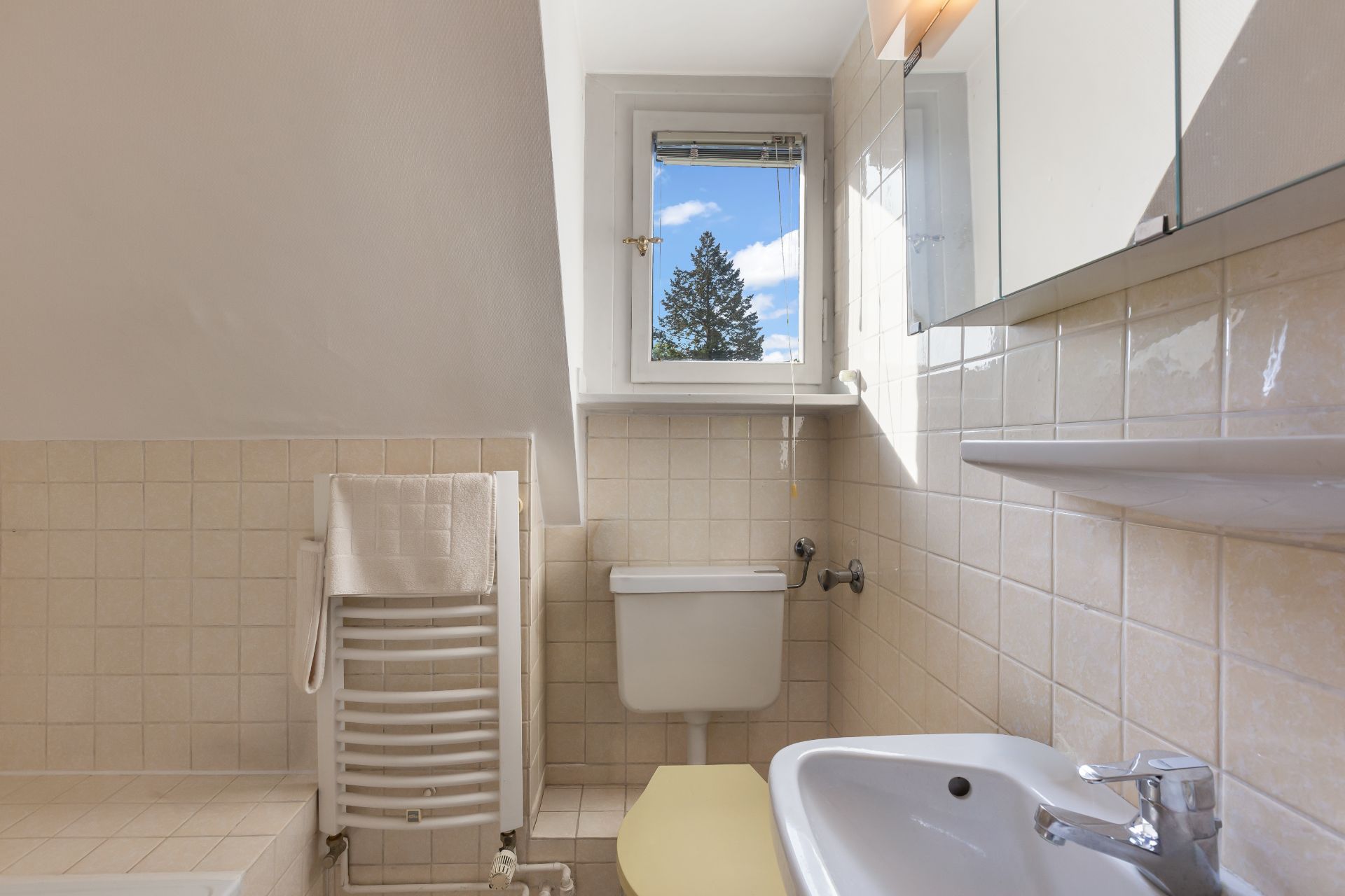 Kleines Badezimmer mit WC, Waschbecken, Heizung und Fenster mit Blick nach draußen.