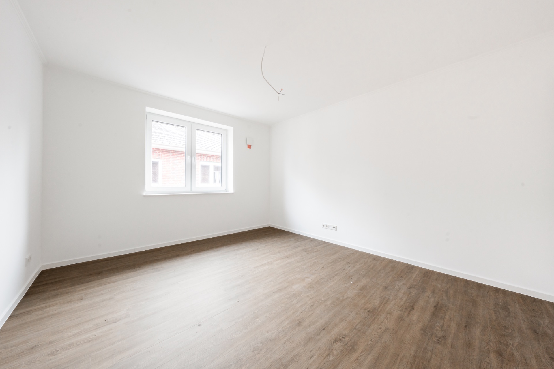 Heller, leerer Raum mit weiß gestrichenen Wänden, Holzfußboden und einem Fenster.