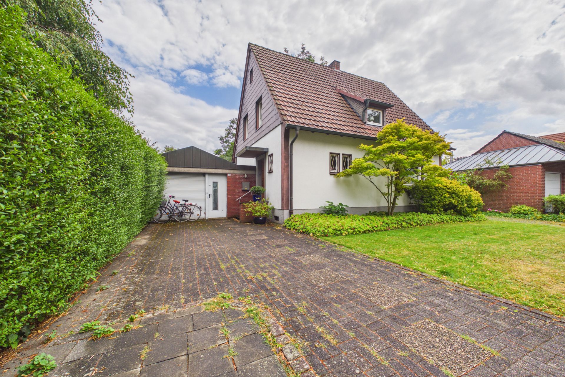 Weiße zweistöckige Wohnhaus mit Satteldach, Auffahrt, Garage und Garten, zwei Fahrräder links.