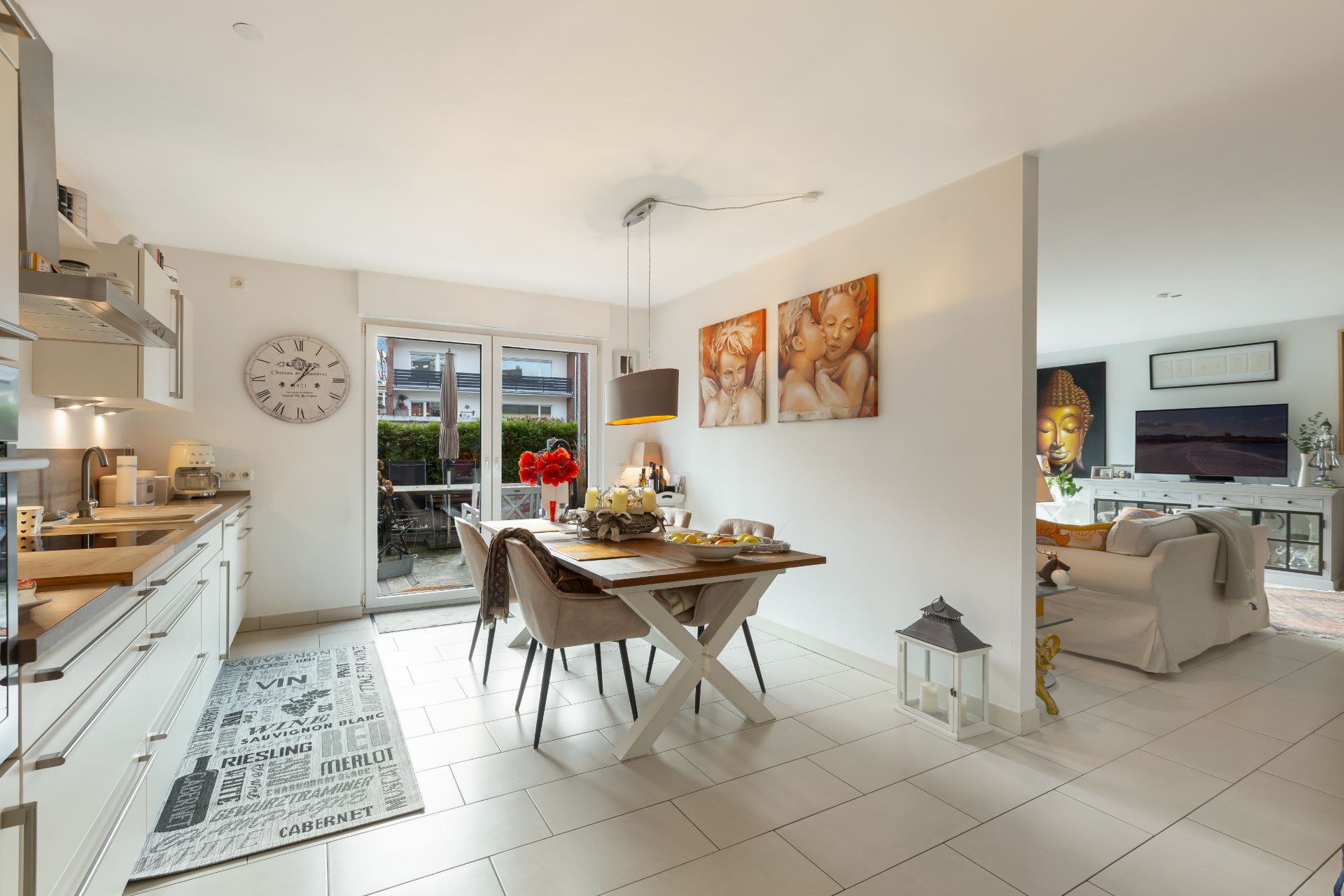 Helle Wohnküche mit Esstisch, Wandbildern und Zugang zur Terrasse, Wohnzimmer im Hintergrund.