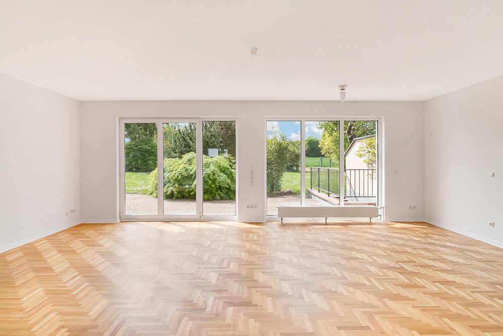 Heller, leerer Raum mit Parkettboden und großen Fenstern zum Garten.