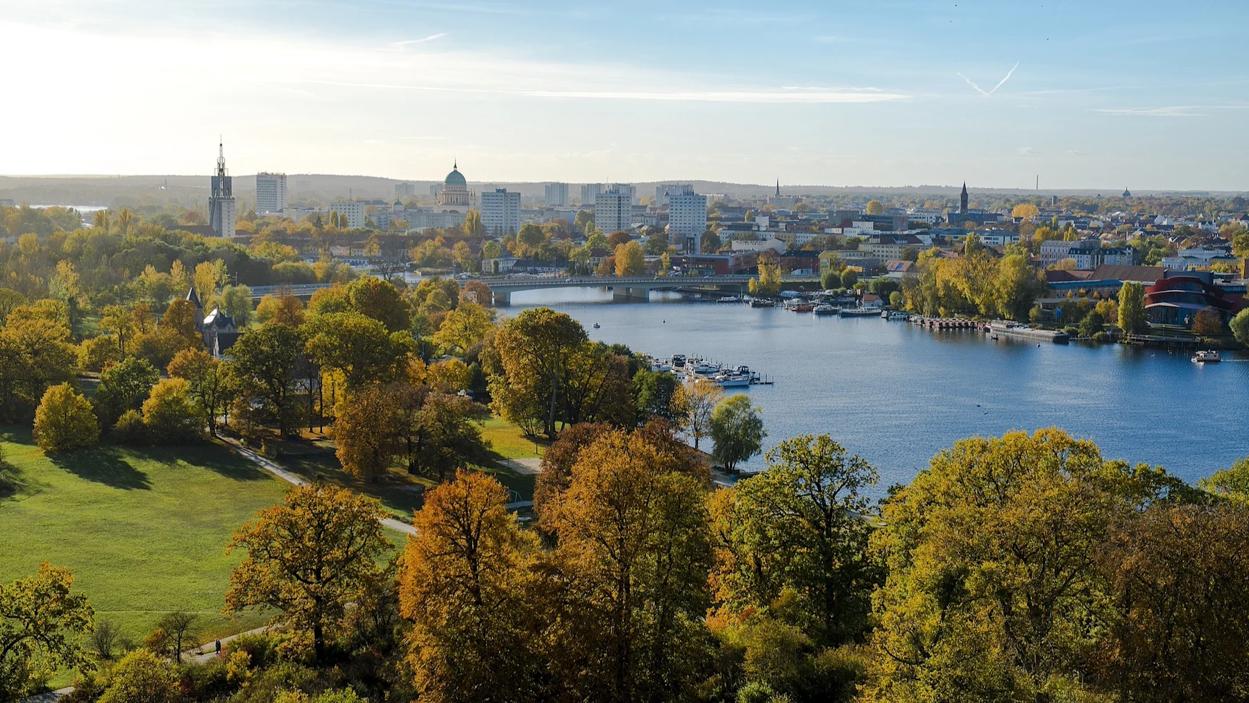 Blick auf eine Stadt mit Fluss, Brücke, vielen Bäumen und Gebäuden im Hintergrund.