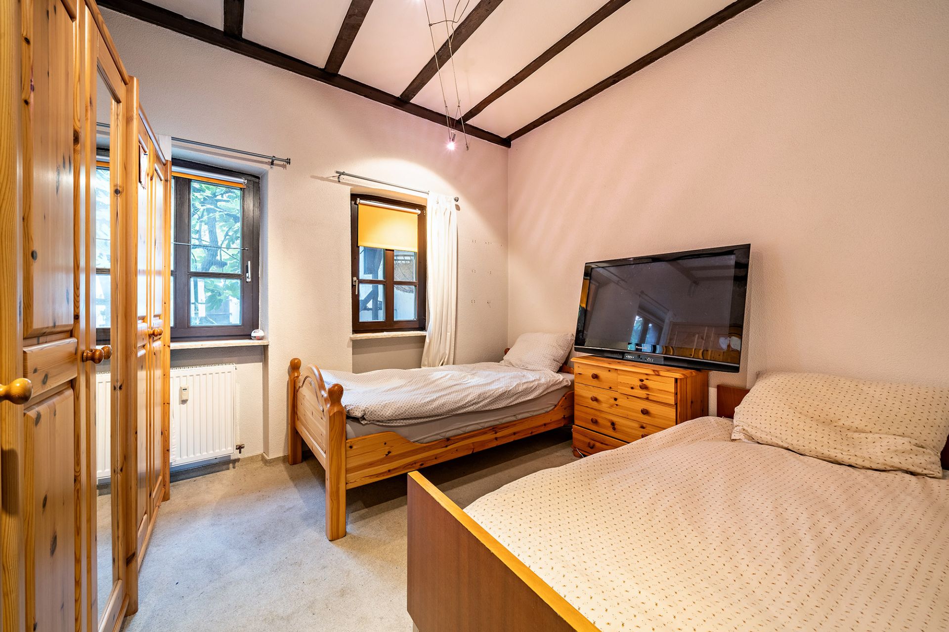 Schlafzimmer mit zwei Einzelbetten, Holzschrank, Kommode und Fernseher.
