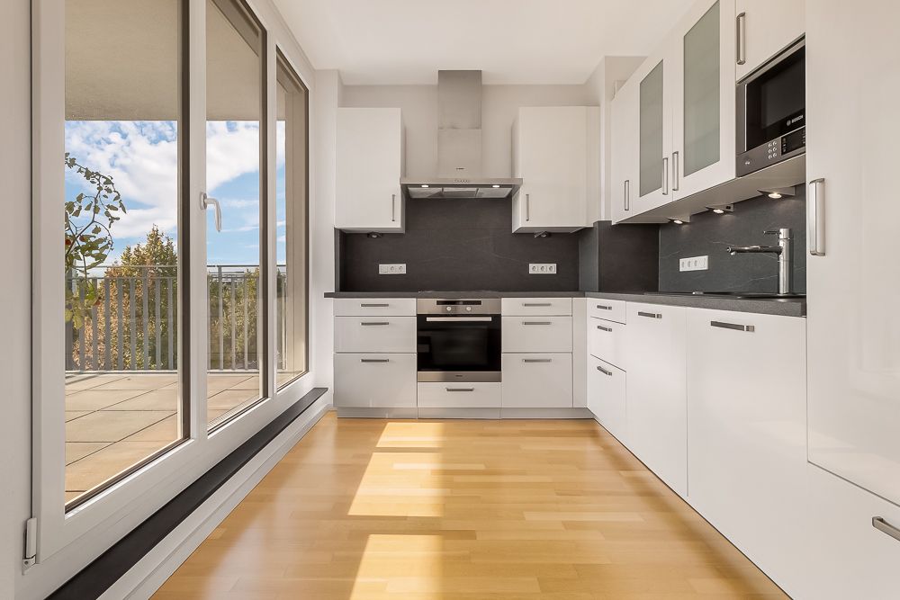 Moderne, helle Einbauküche mit weißen Schränken und großem Fenster zur Terrasse.