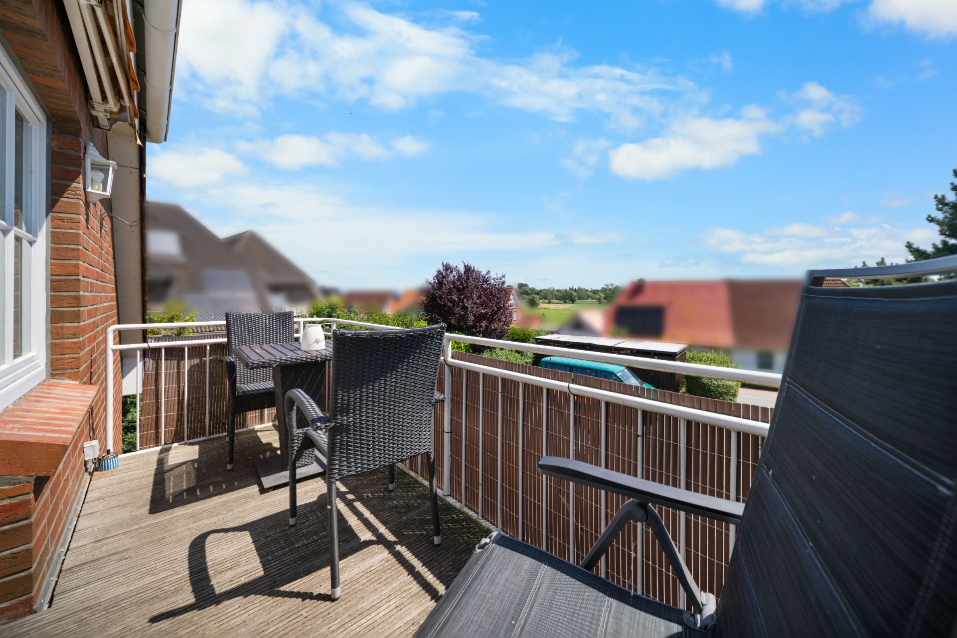 Balkon mit zwei schwarzen Stühlen und Tisch, Blick auf Garten und Nachbarhäuser.