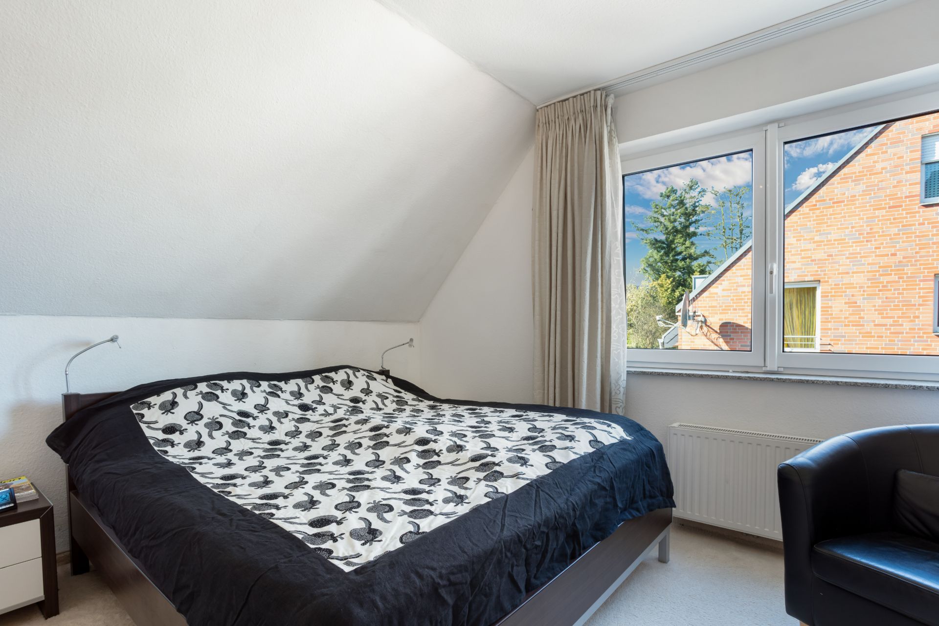 Schlafzimmer mit Doppelbett, Nachttisch, Sessel und großem Fenster mit Blick nach draußen.