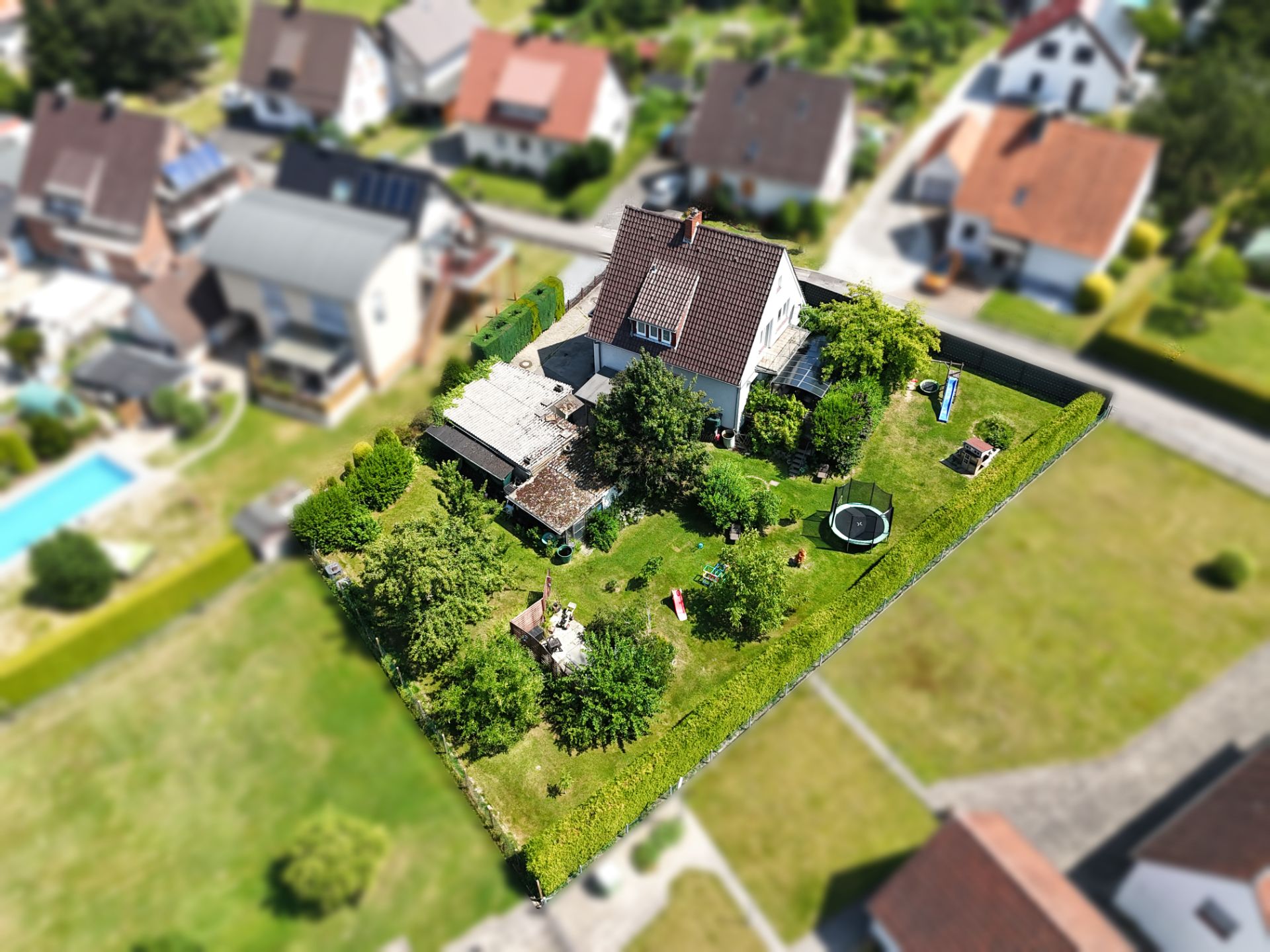 Luftaufnahme eines Hauses mit großem Garten, Bäumen und Trampolin im Wohngebiet.