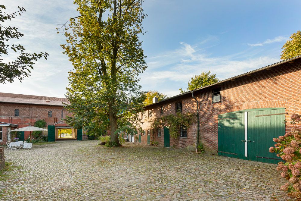Gepflasterter Innenhof mit großem Baum, Backsteingebäuden und grünen Türen.