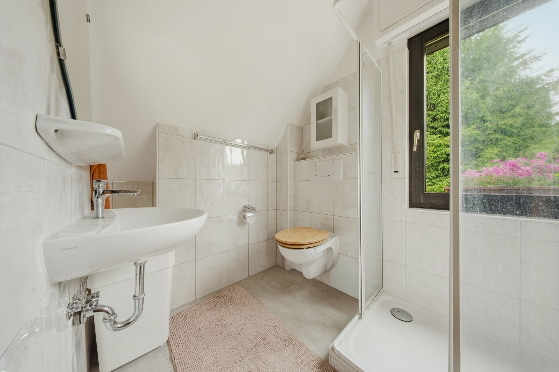 Helles Badezimmer mit Dusche, Waschbecken, WC und Fenster mit Blick ins Grüne.