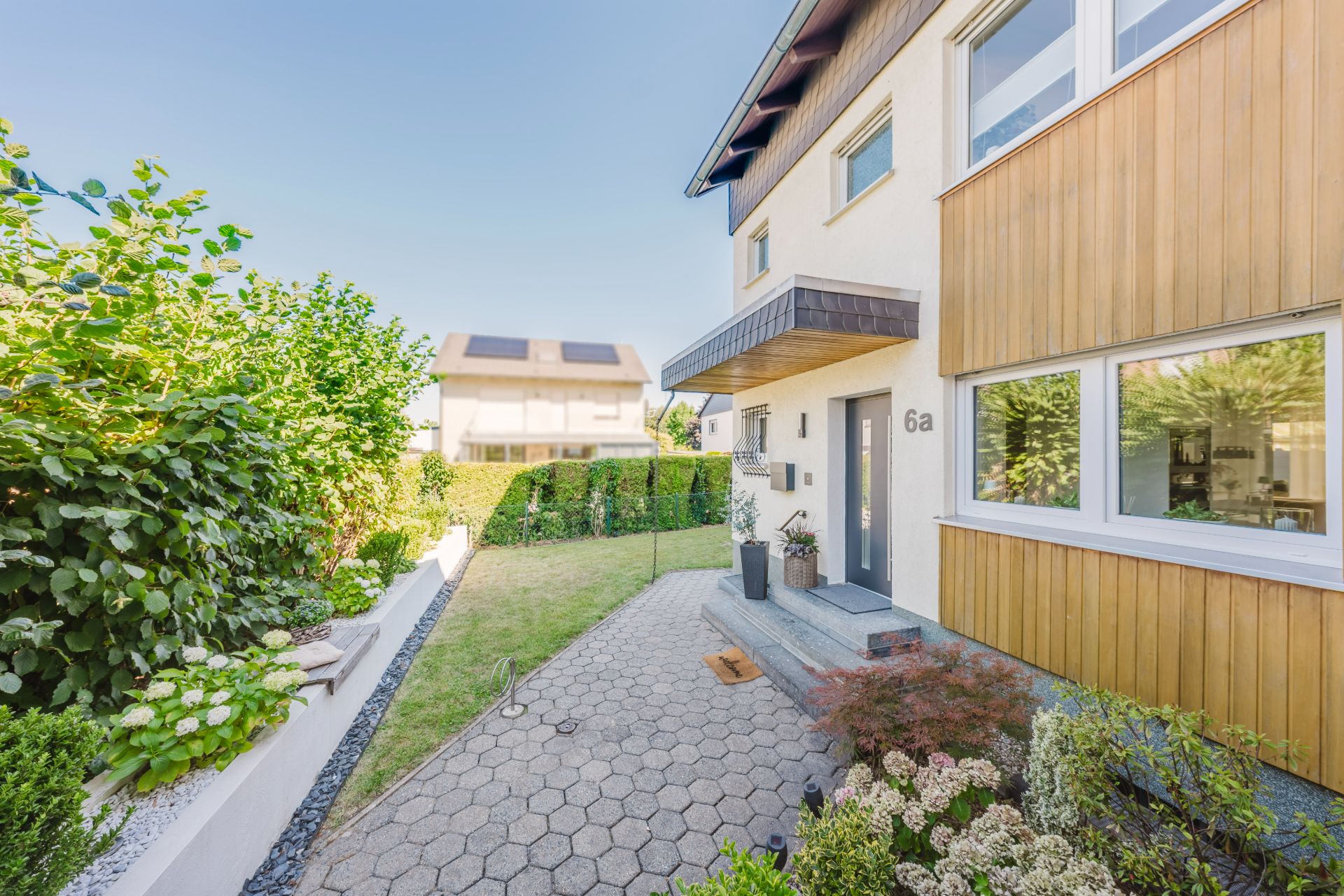 Eingangsbereich eines modernen Wohnhauses mit gepflastertem Weg und kleinem Vorgarten.