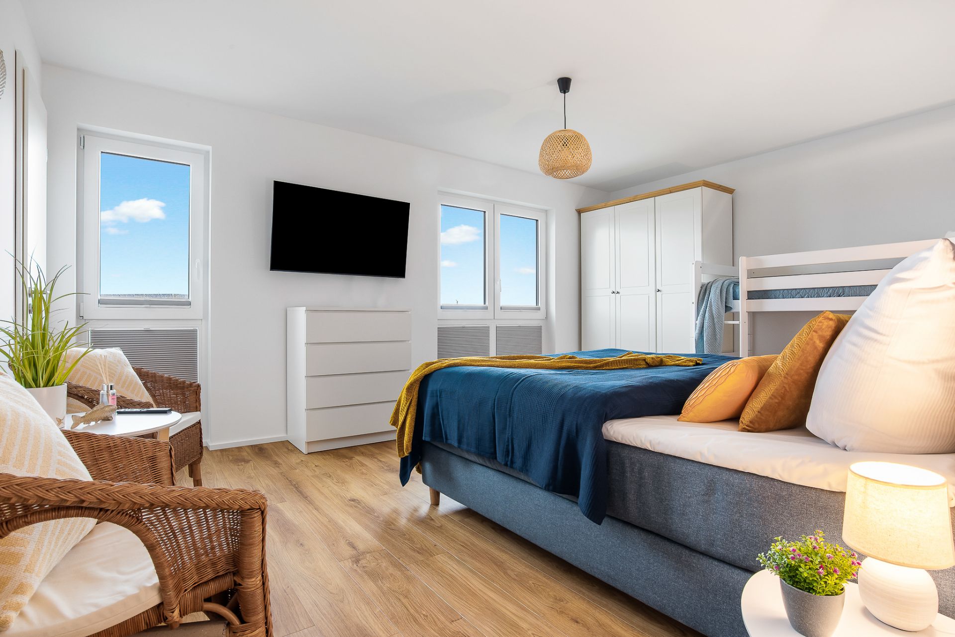 Helles Schlafzimmer mit Doppelbett, TV, Kleiderschrank, Sitzbereich und Holzboden.