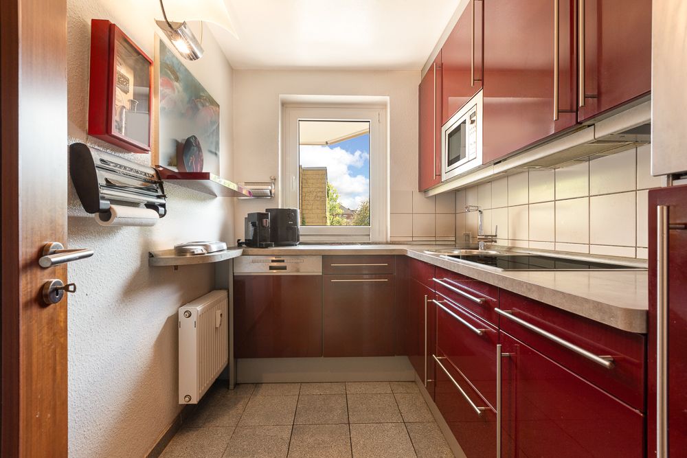 Moderne Küche mit roten Schränken, Fenster, Spüle, Herd und Kaffeemaschine.