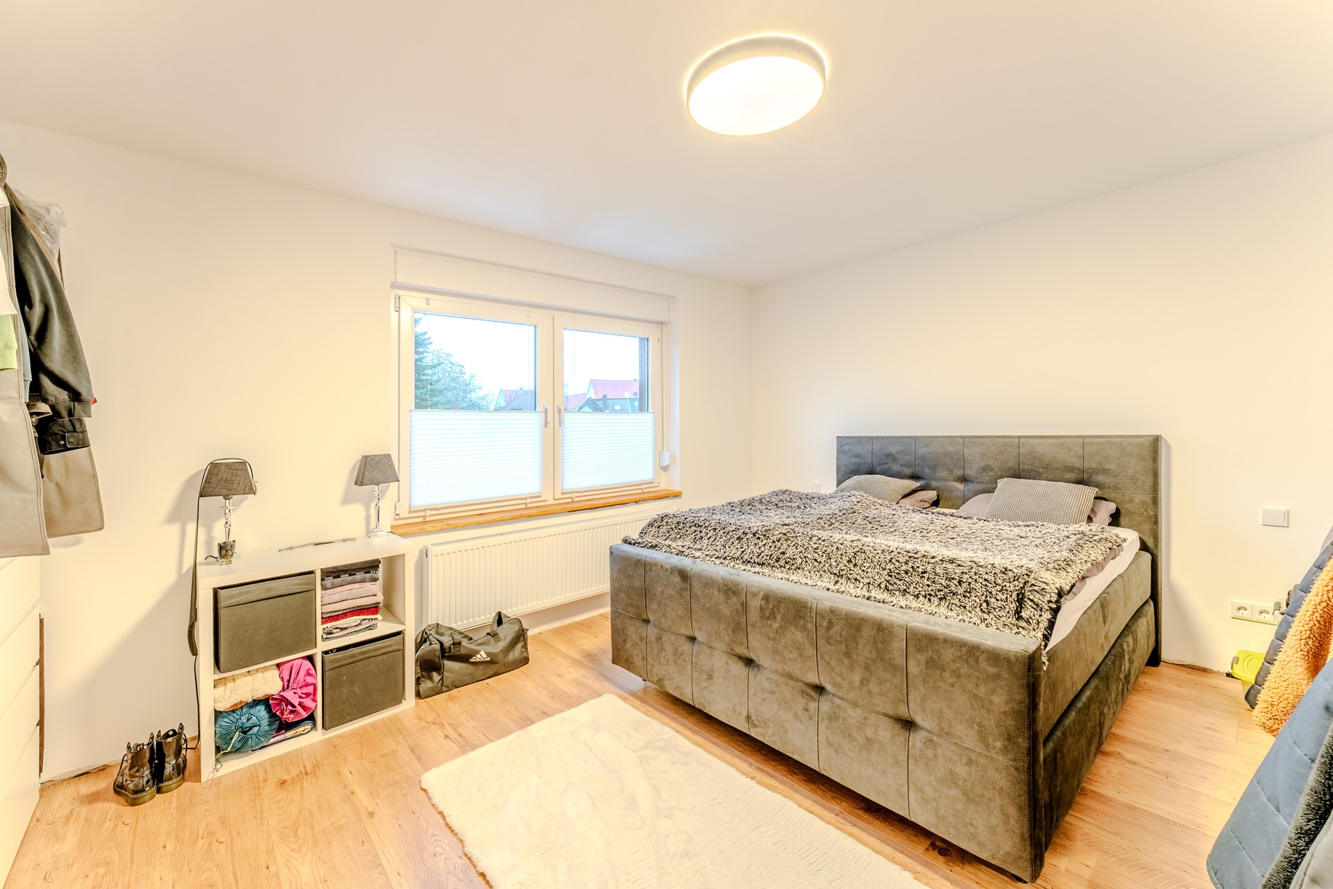 Helles Schlafzimmer mit großem Bett, zwei Fenstern und einem Regal neben dem Bett.