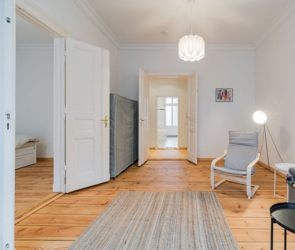 Helles Wohnzimmer mit Holzfußboden, Teppich, Sessel, Stehlampe und offenen Türen zu weiteren Räumen.