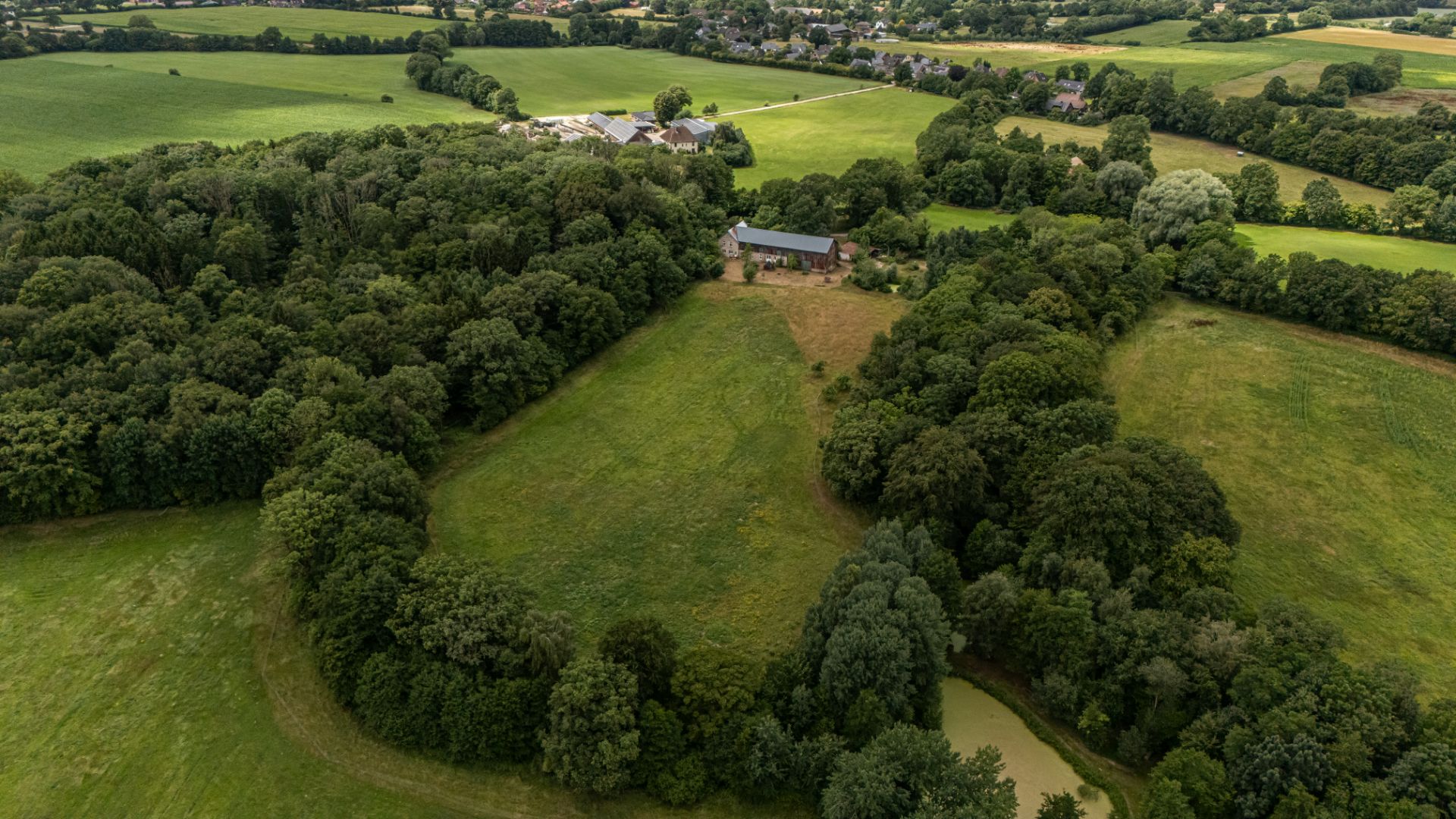 Luftaufnahme eines Hauses mitten in grüner Landschaft mit Wäldern und Wiesen.