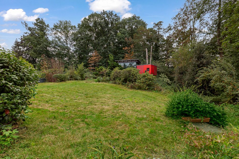 Großer grüner Garten mit Rasen, Büschen und einem roten kleinen Gebäude im Hintergrund.