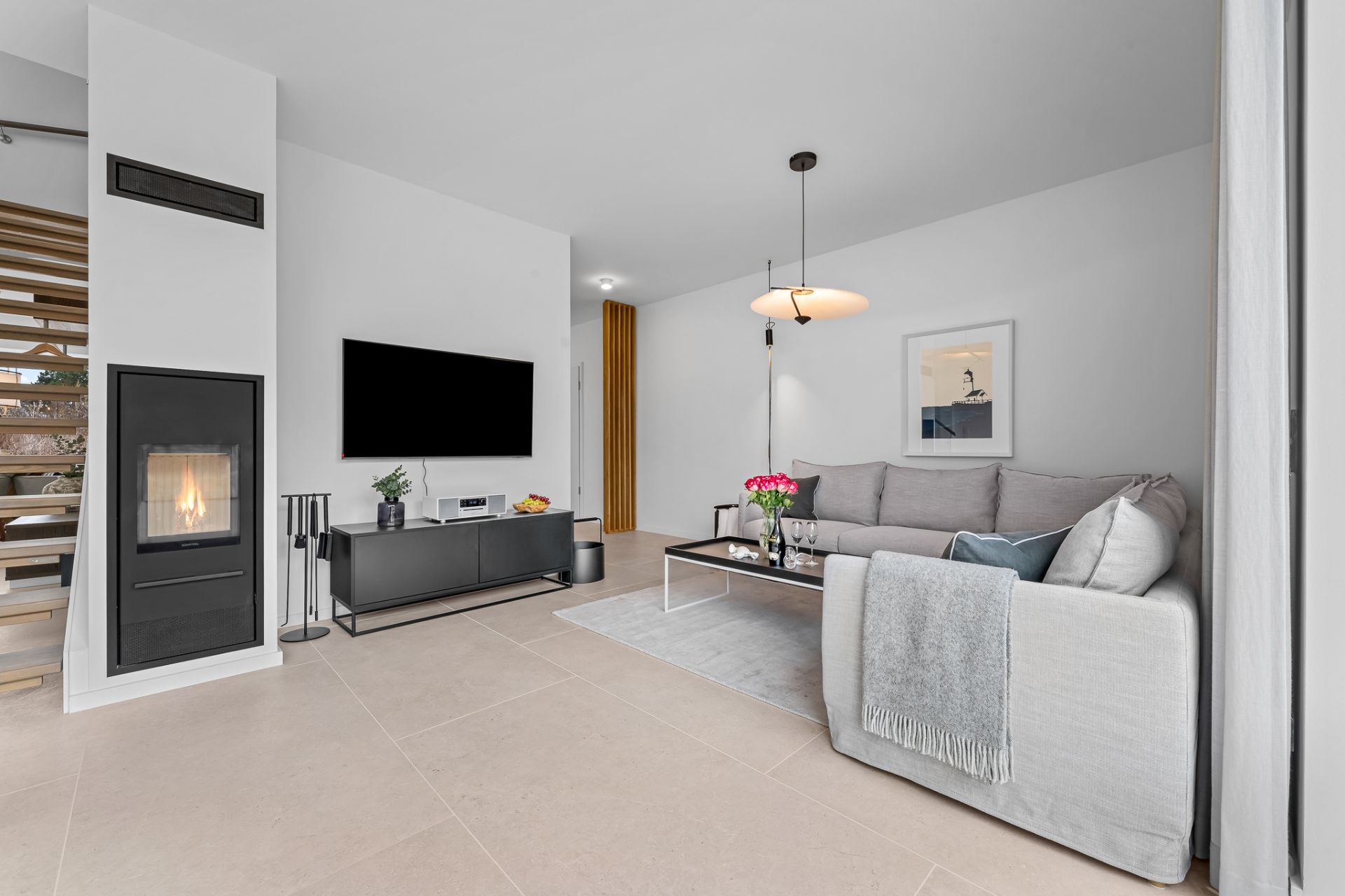 Modernes Wohnzimmer mit Kamin, grauem Sofa, Couchtisch, TV und Treppe im Hintergrund.