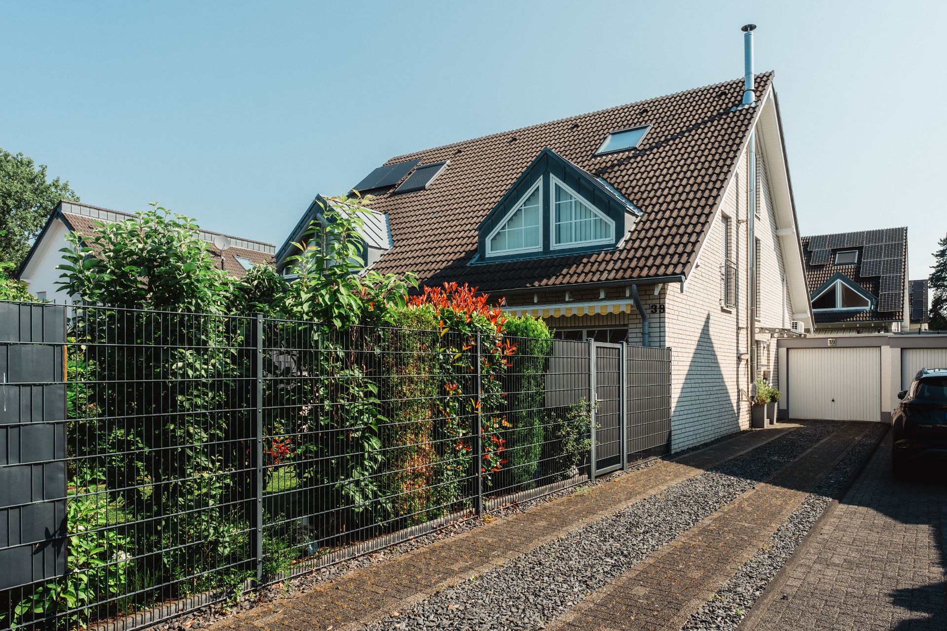 Modernes Einfamilienhaus mit Gartenzäunen, Pflanzen und Garage bei sonnigem Wetter.