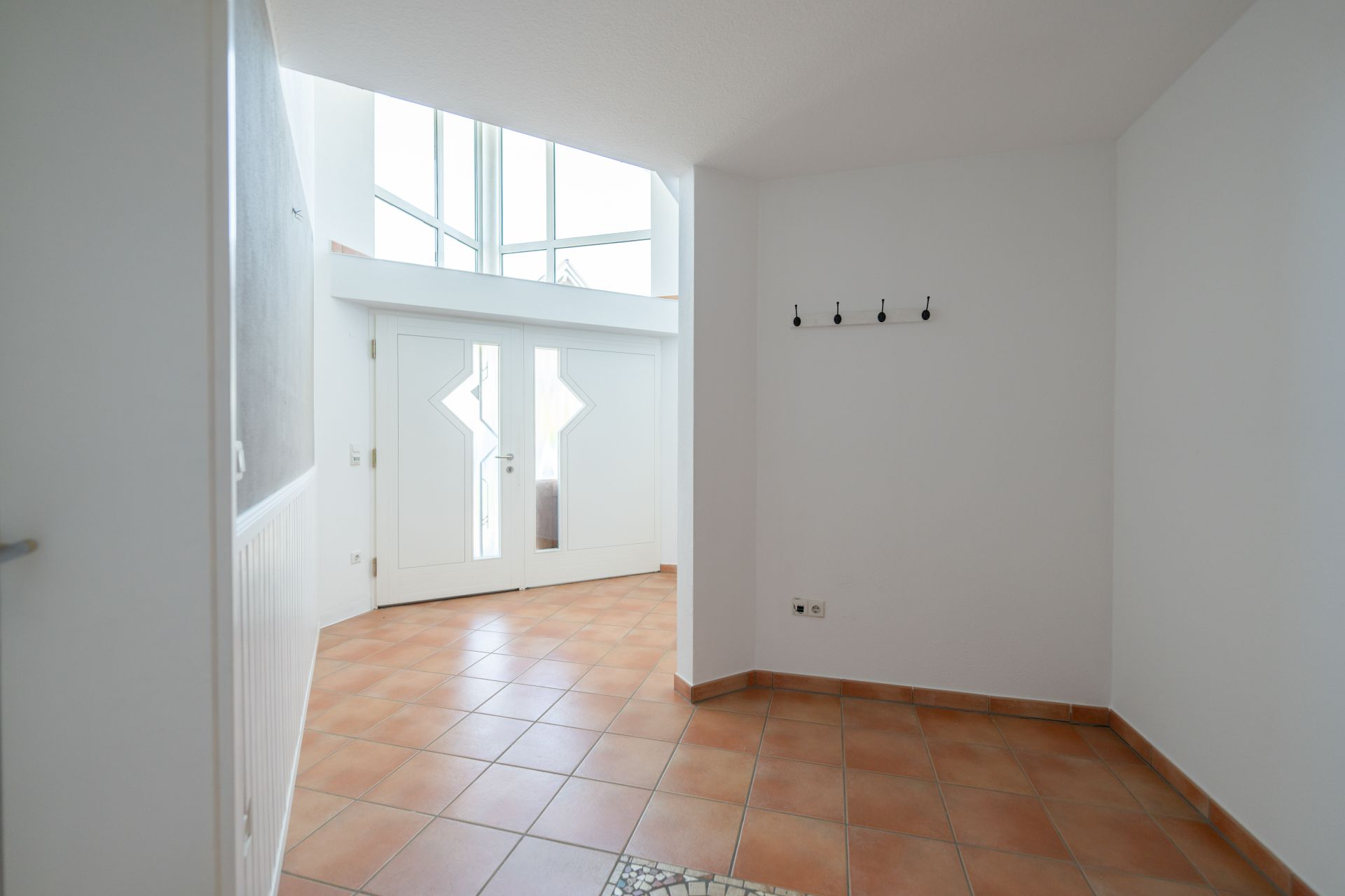 Heller Flur mit weißen Wänden, Fliesenboden und Garderobenhaken an der Wand.