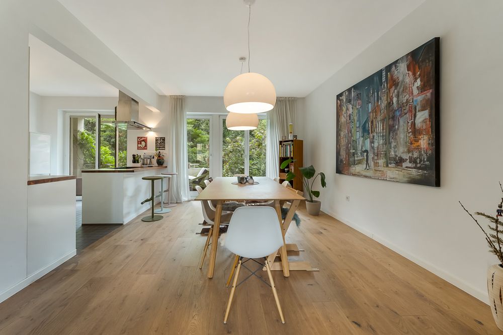 Helles Esszimmer mit Holzboden, großem Gemälde, Esstisch und Blick in eine moderne Küche.