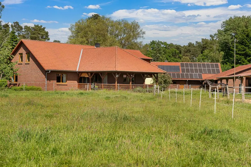 Backsteinhaus mit rotem Dach, großer überdachter Terrasse und Wiese im Vordergrund.