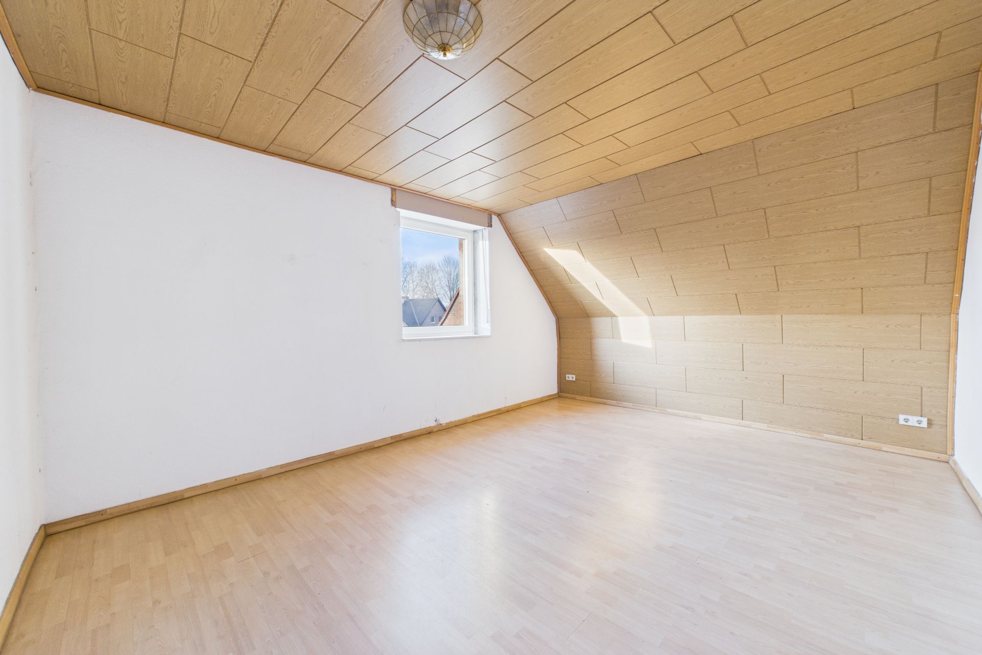 Helles, leeres Zimmer mit Holzdecke, Holzfußboden und einem Fenster an der Seitenwand.