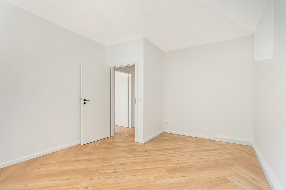 Leerer, heller Raum mit Holzfußboden und weißer Tür, die ins nächste Zimmer führt.