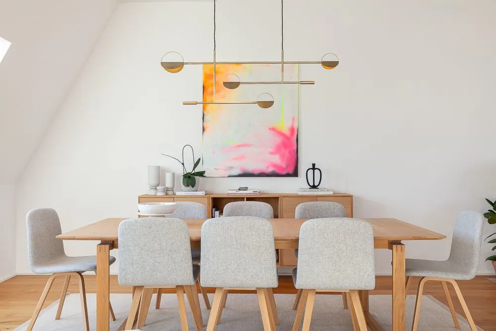 Esszimmer mit Holztisch, acht grauen Stühlen und buntem Bild an der Wand.