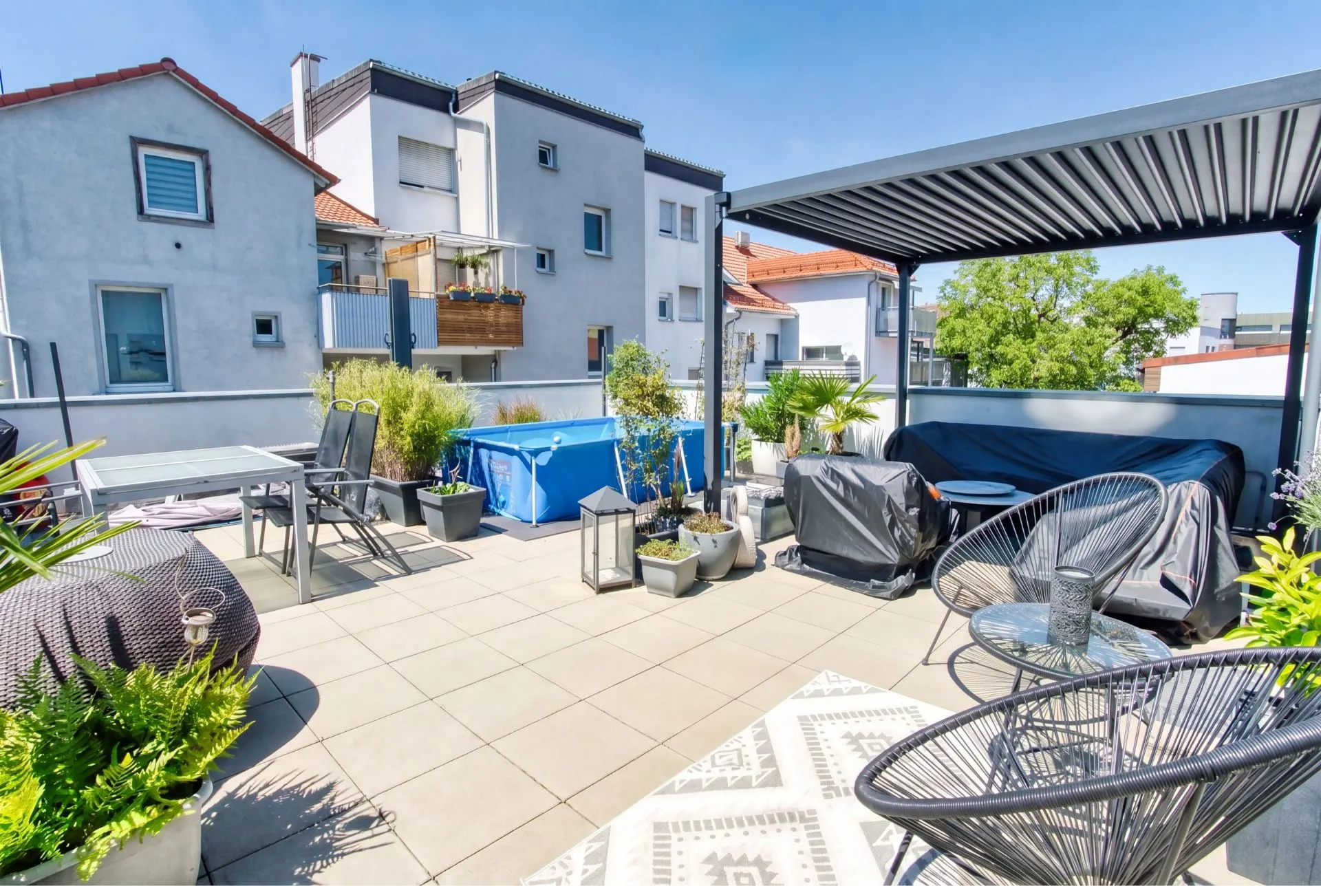 Große Dachterrasse mit Sitzmöbeln, Pflanzen, Pool und Pergola in einem Wohngebiet.