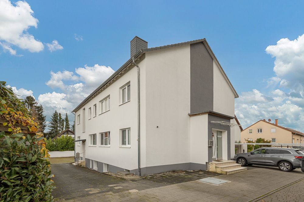 Zweistöckiges Wohnhaus mit weißer Fassade, Eingangsbereich und geparktem Auto vor dem Haus.
