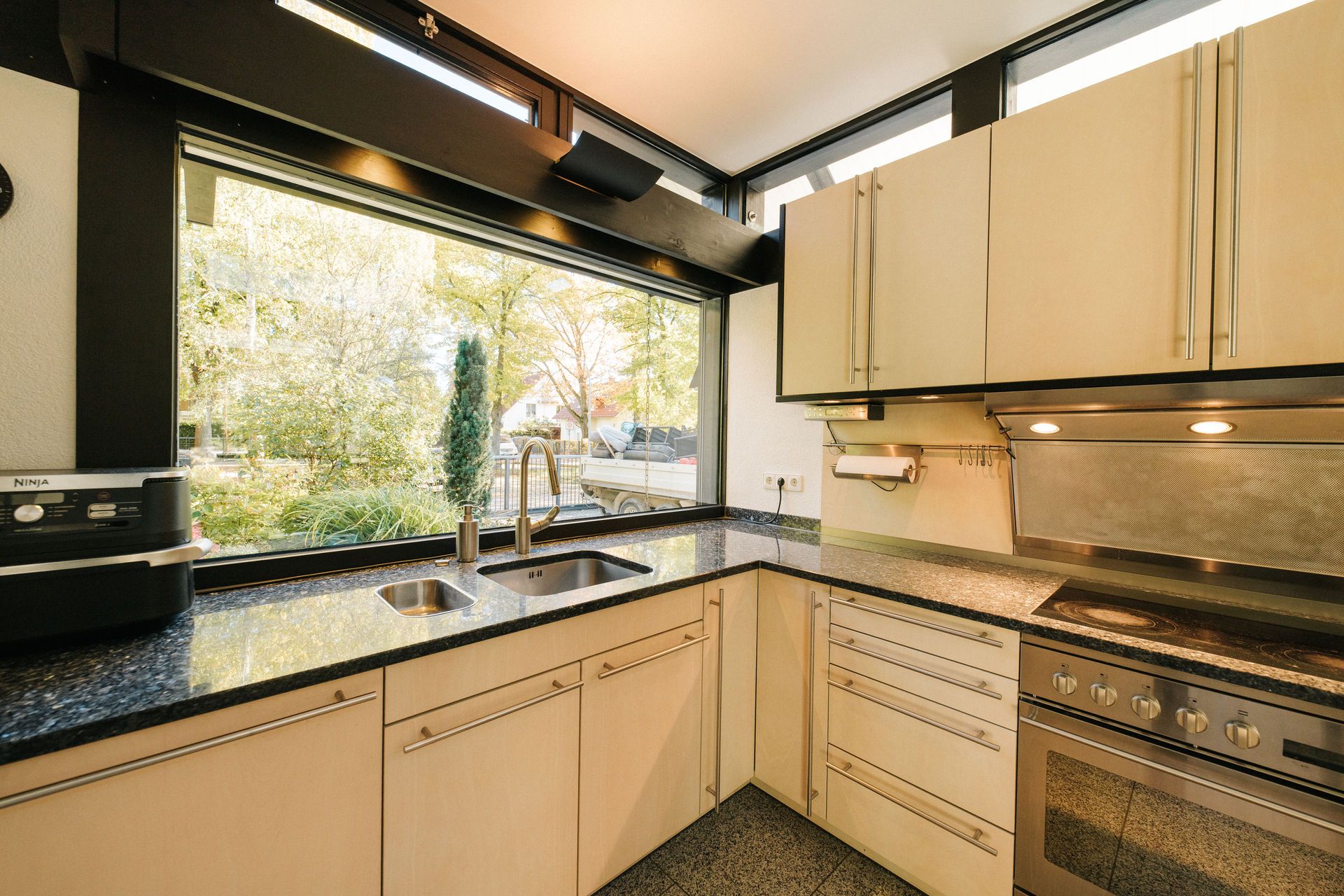 Moderne Küche mit Eckfenster, Spüle, Herd, hellen Schränken und Granit-Arbeitsplatte.