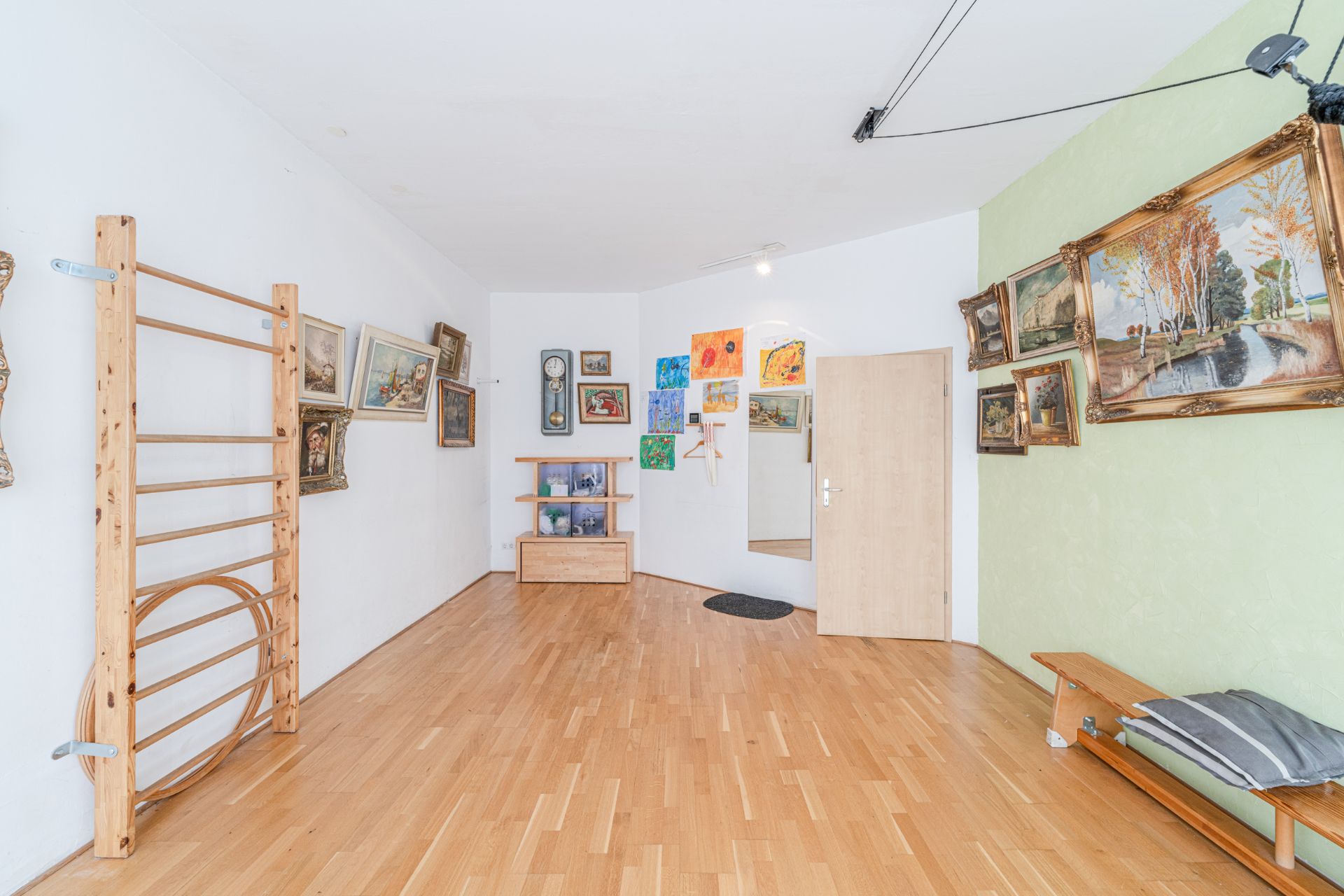Raum mit Holzsprossenwand, Bildern an den Wänden, Holzbank und Spiegel.