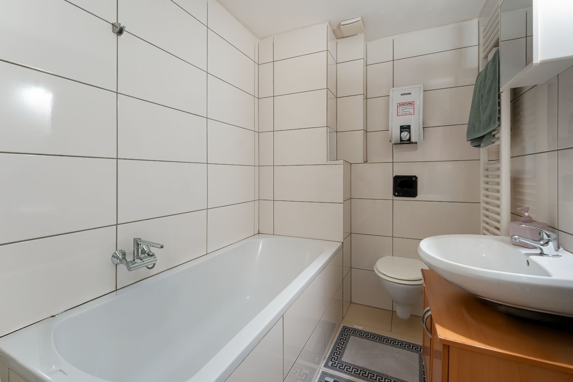 Modernes Badezimmer mit Badewanne, Waschbecken, WC und weißen Wandfliesen.