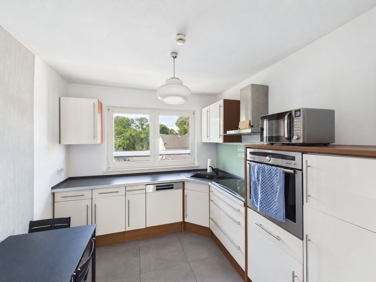 Moderne Einbauküche mit weißen Schränken, großem Fenster, Ofen und Mikrowelle.
