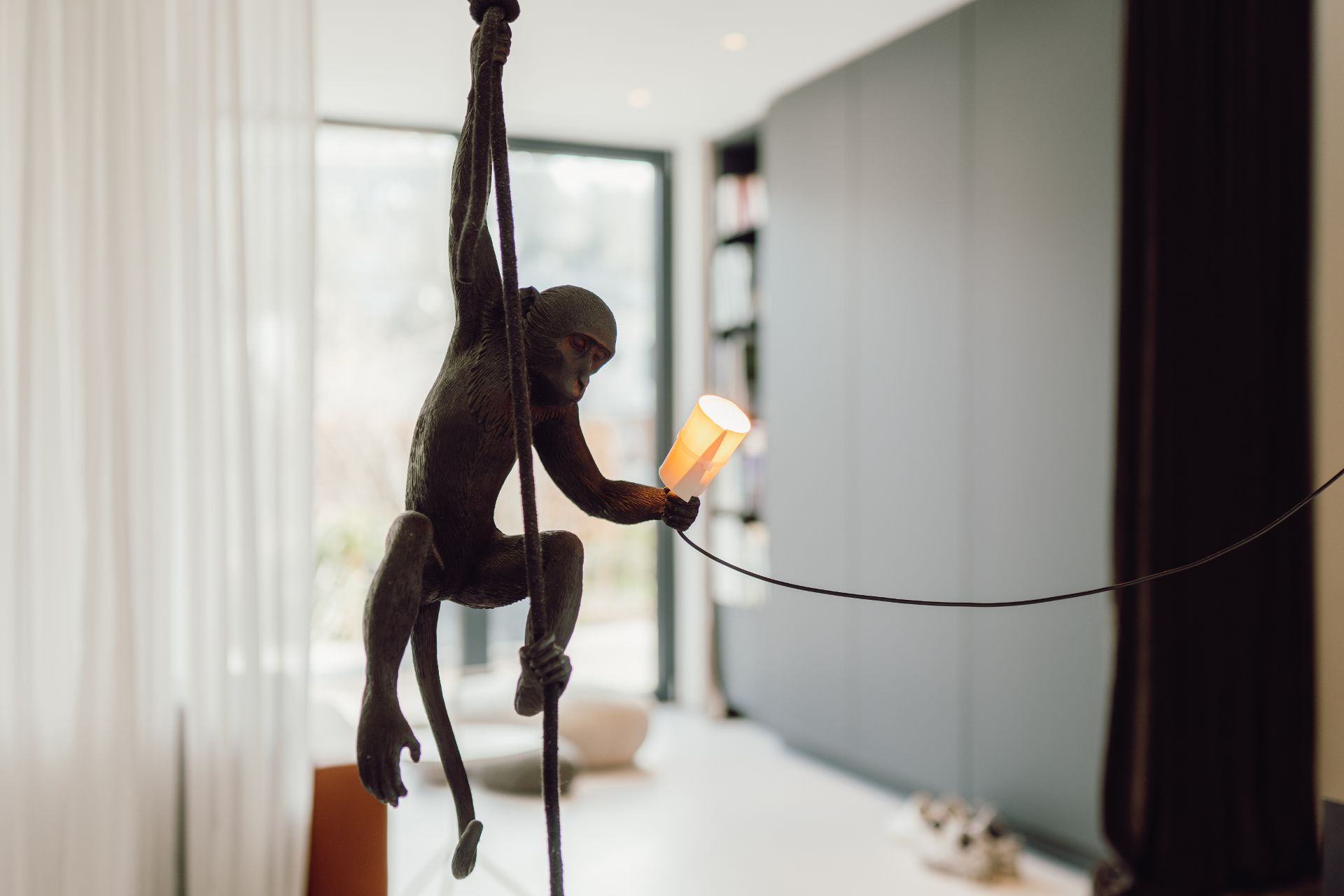 Affenskulptur mit Lampe in der Hand hängt an einem Seil in modernem Wohnraum.